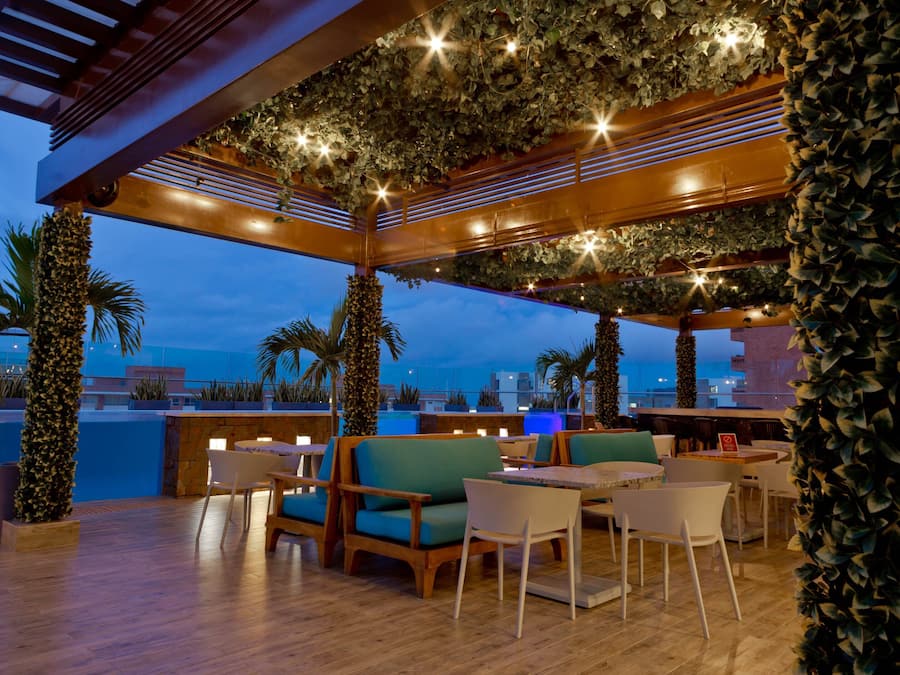 Een terras met houten tafels en stoelen, omgeven door groen en uitzicht op de oceaan.