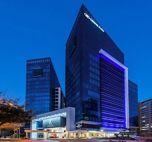 A modern hotel with a prominent 'Crowne Plaza' sign, featuring a sleek glass facade and a distinctive blue-lit entrance.
