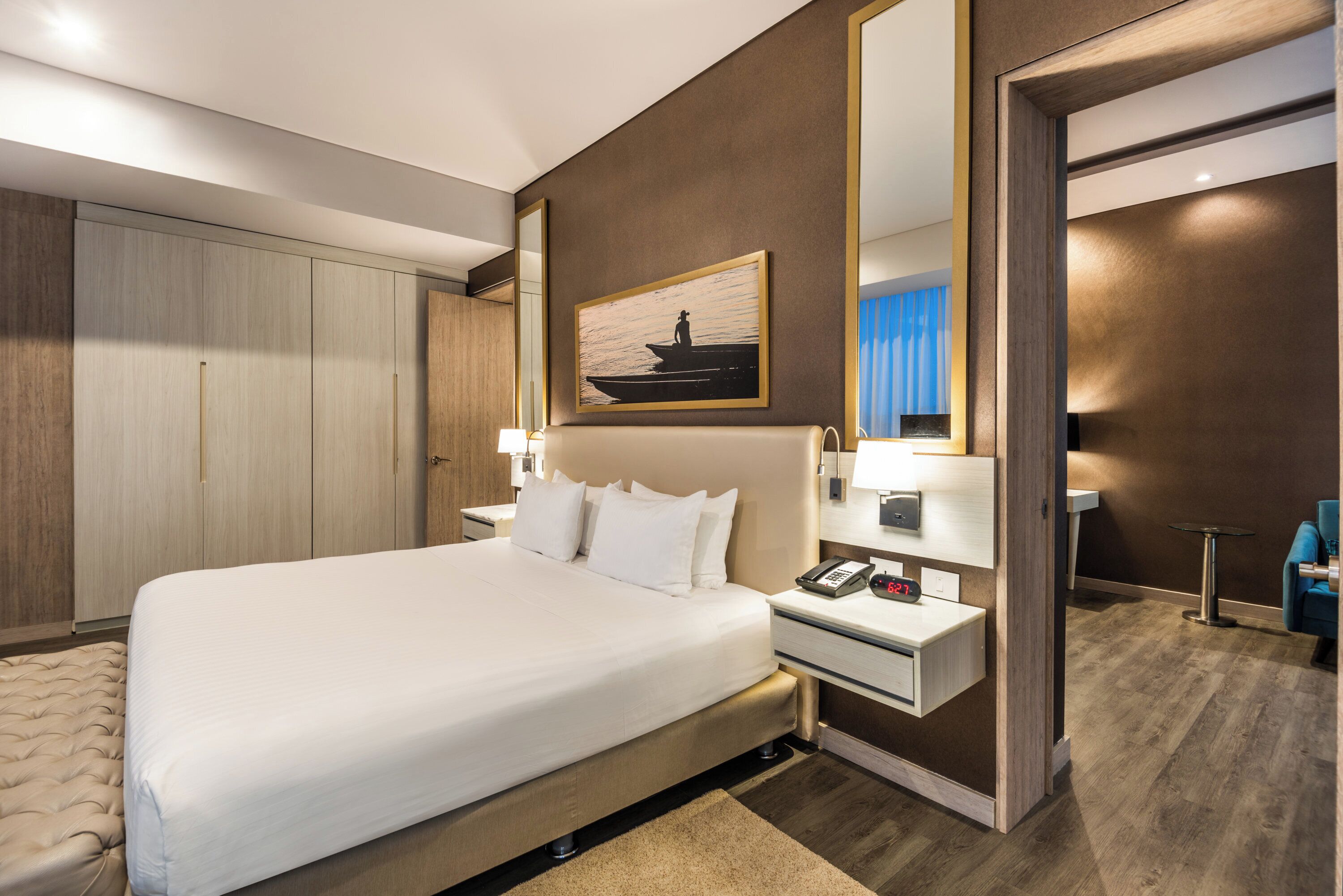 A hotel room with a large bed, bedside tables, a mirror, and a painting on the wall.