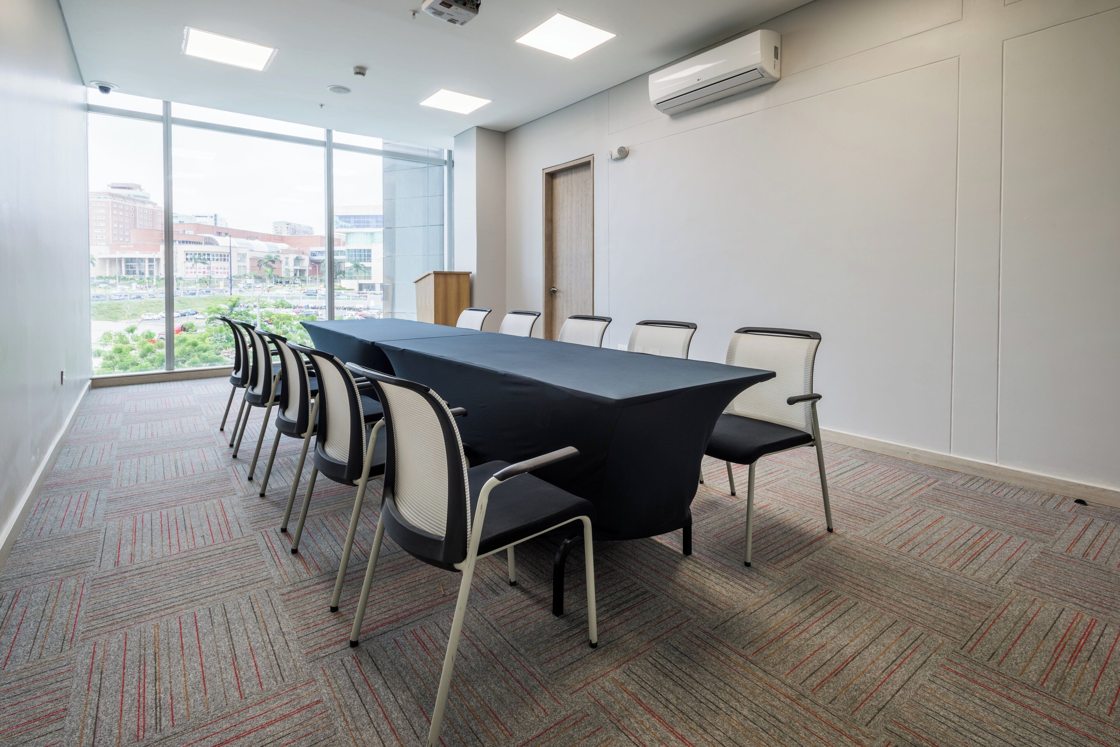 A conference room with a long table, six chairs, and a large window with a view of buildings.
