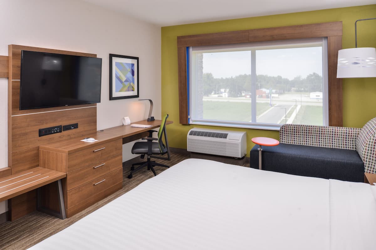 A hotel room with a bed, desk, chair, TV, air conditioner, and a window with a view.