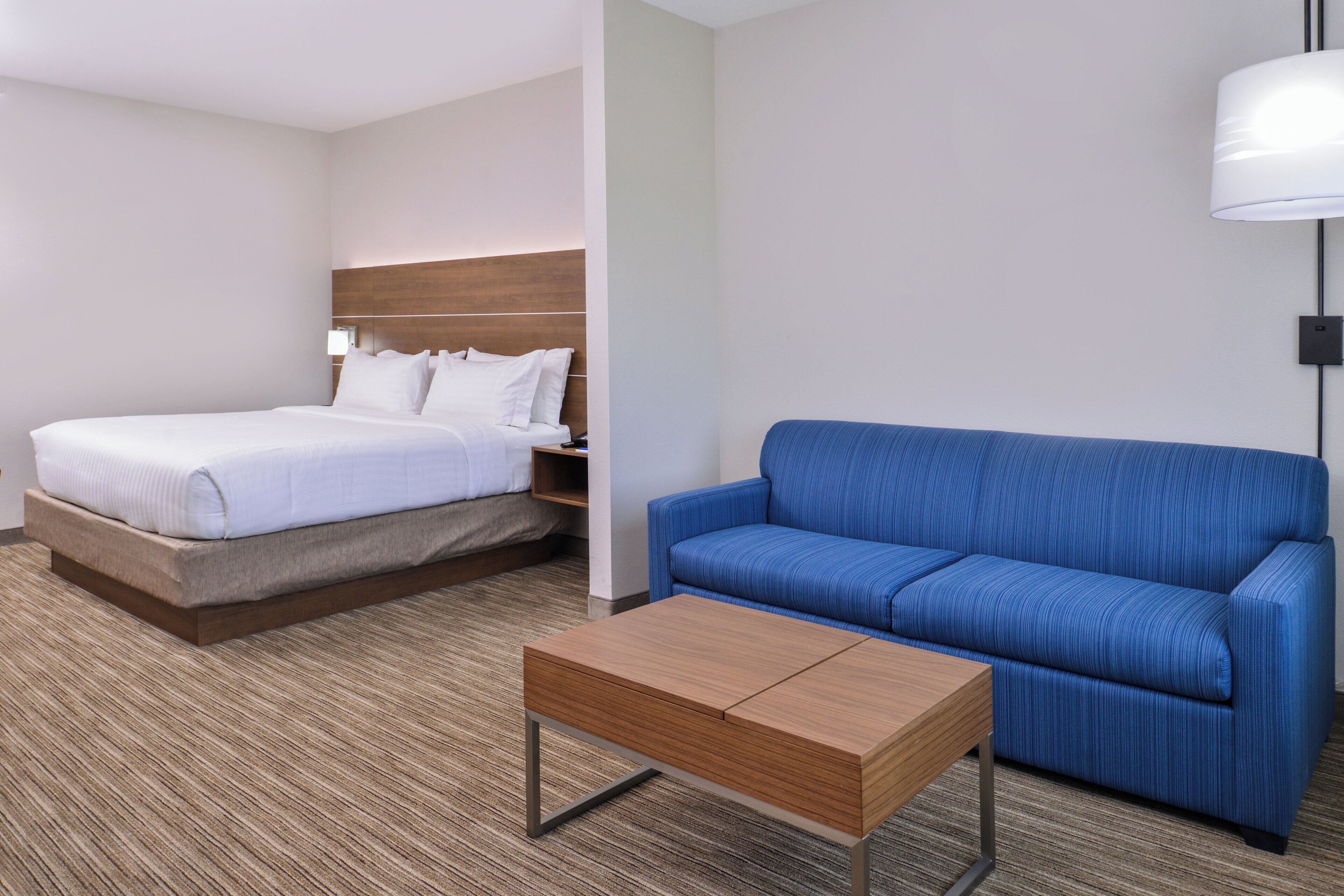 A hotel room with a bed, a blue sofa, and a wooden coffee table.