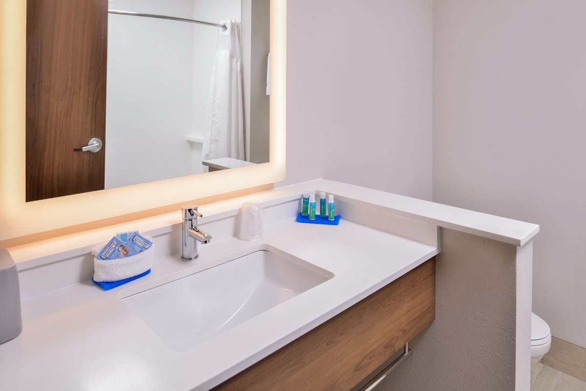 A bathroom with a white sink, wooden vanity, and a mirror with a lighted frame.