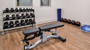 Un gimnasio con banco, mancuernas y pelotas de ejercicio.
