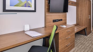 Una habitación de hotel con un escritorio de madera, una silla, un televisor fijado a la pared y un cuadro enmarcado sobre el escritorio.