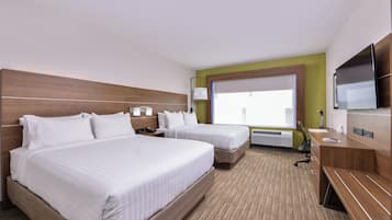 A hotel room with two beds, a TV, a desk, and a window with blinds.