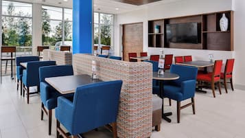 Un restaurante moderno con asientos azules y rojos, ventanas amplias y un televisor de pantalla plana en la pared.