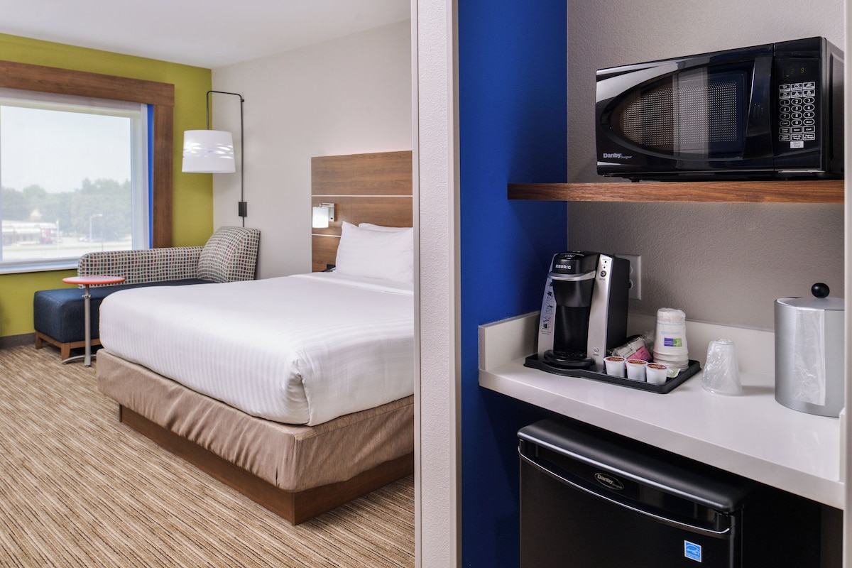Habitación de hotel con cama, escritorio, microondas, cafetera y artículos de aseo.