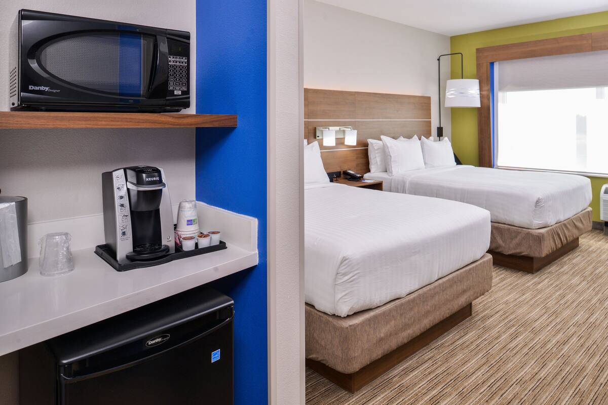 A hotel room with a microwave, coffee maker, and a small refrigerator on the counter. There are two beds with white linens and a window with a view.