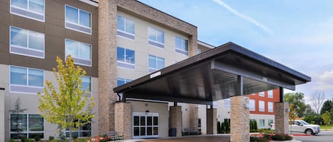 Un hotel de varios pisos con entrada cubierta, fachada de piedra y estacionamiento.