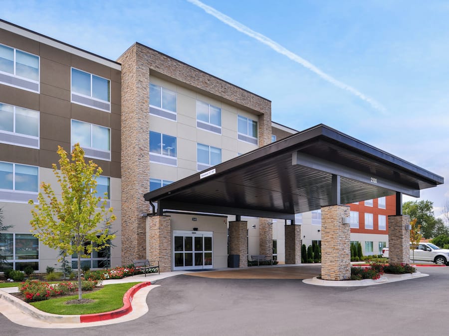 A multi-story hotel with a covered entrance, stone facade, and a parking lot.