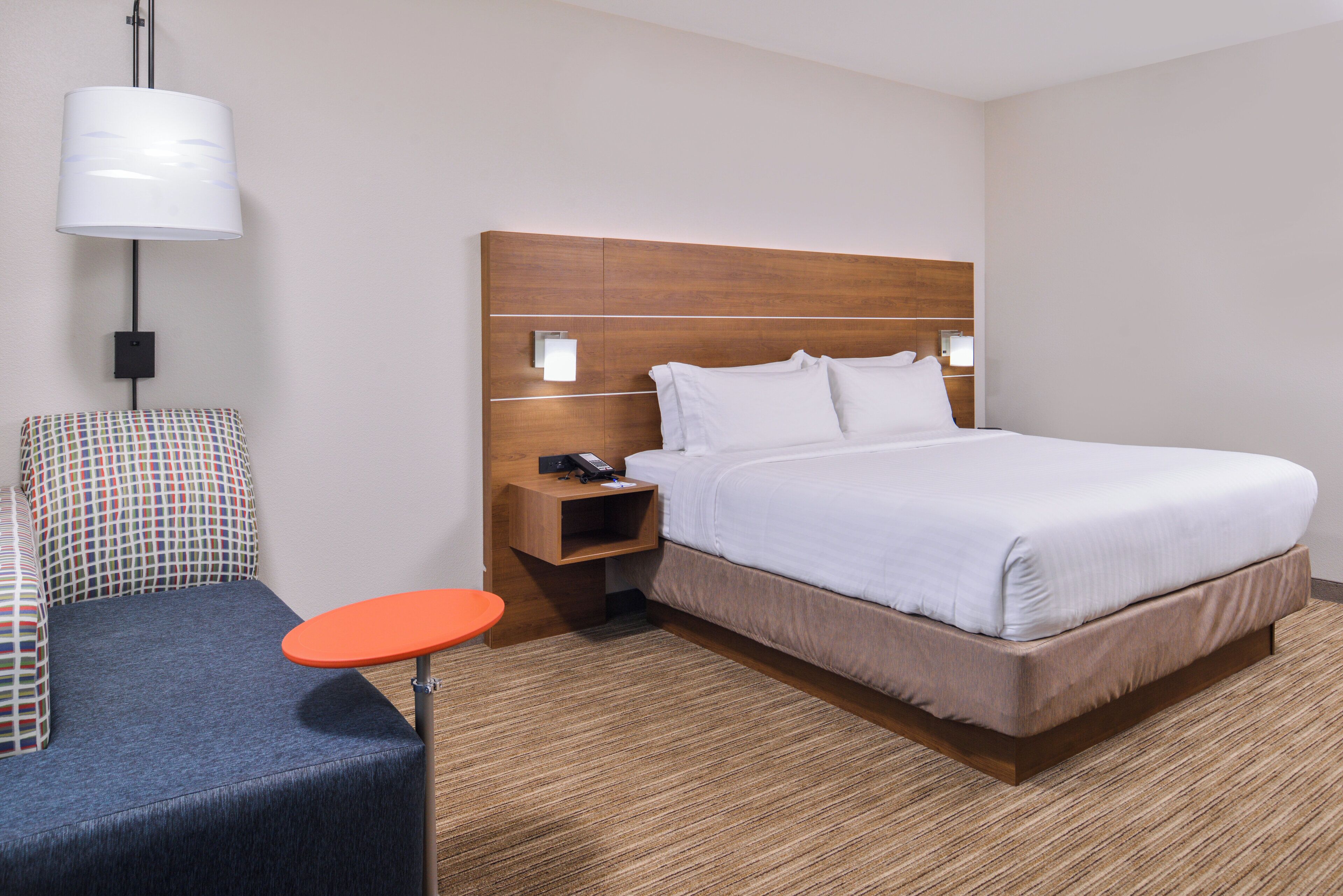Een hotelkamer met een bed, nachtkastje, telefoon, lamp, stoel en een klein tafeltje.
