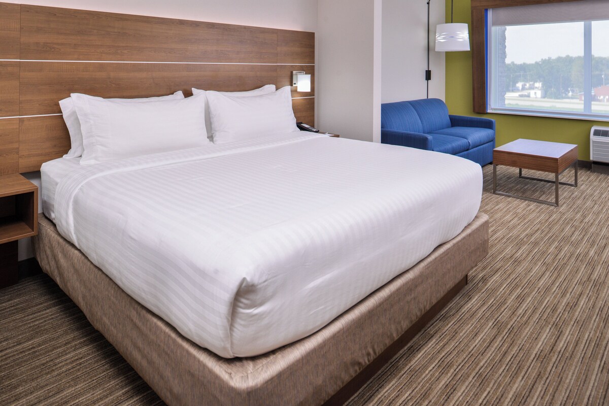 A hotel room with a large bed, a blue armchair, a small table, and a window with a view.