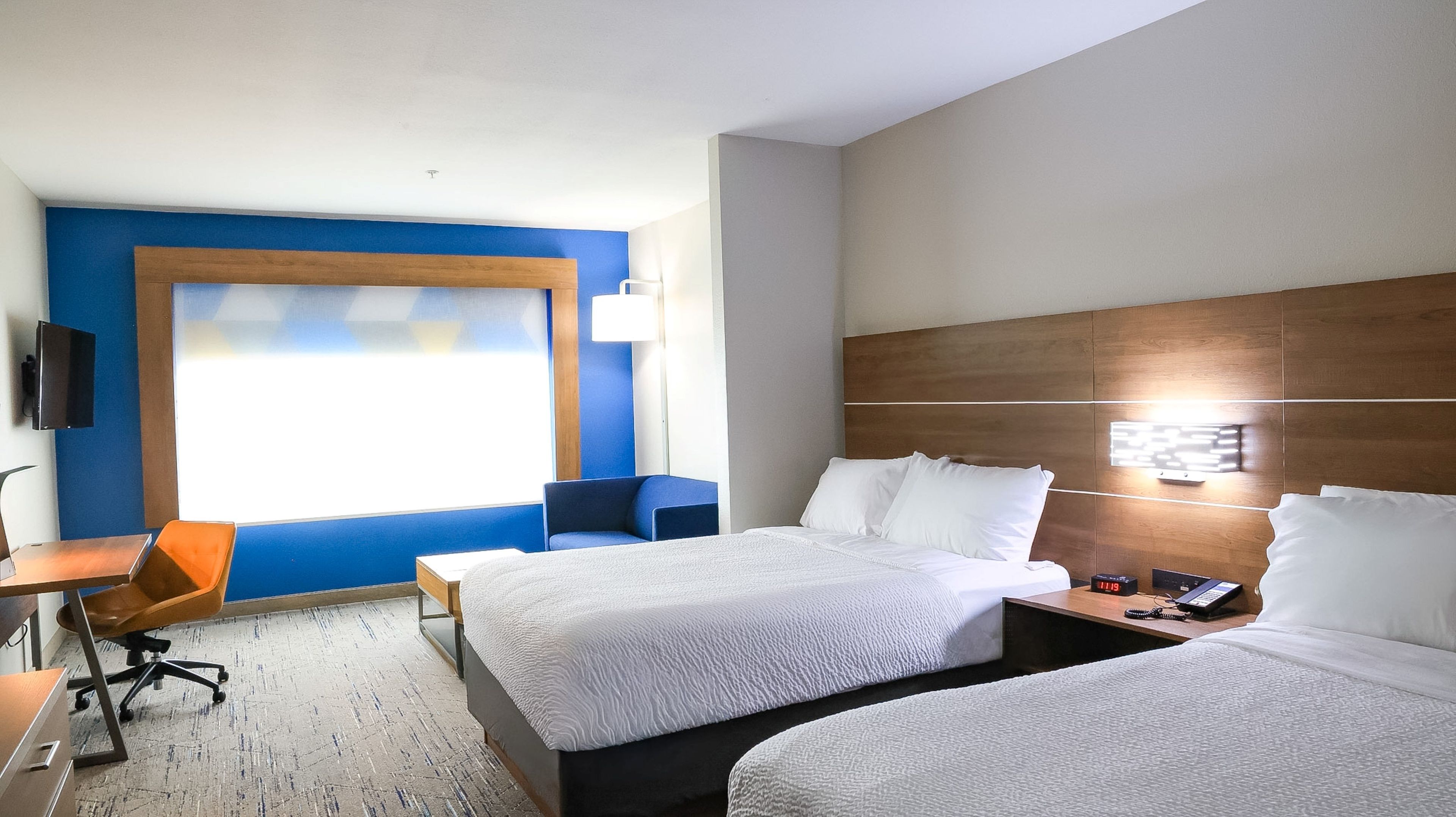 A hotel room with two beds, a desk, a chair, a TV, and a bedside table with a phone.