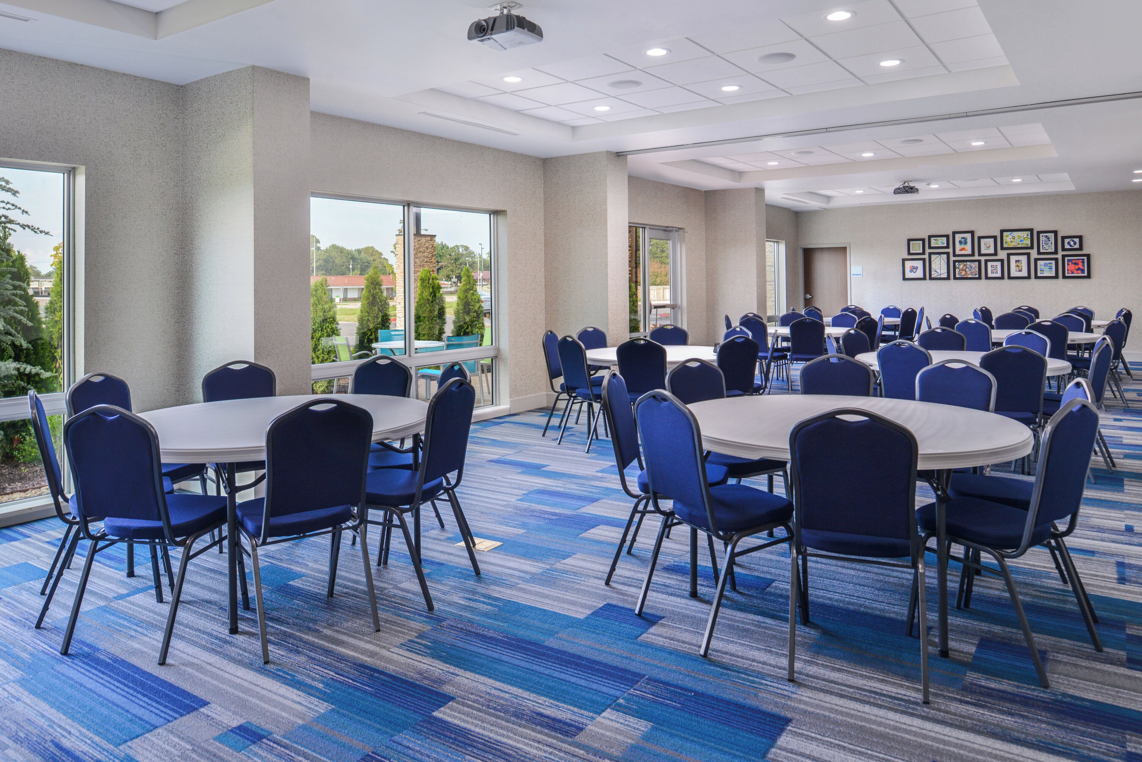 A conference room with round tables and chairs, large windows, and a carpeted floor.