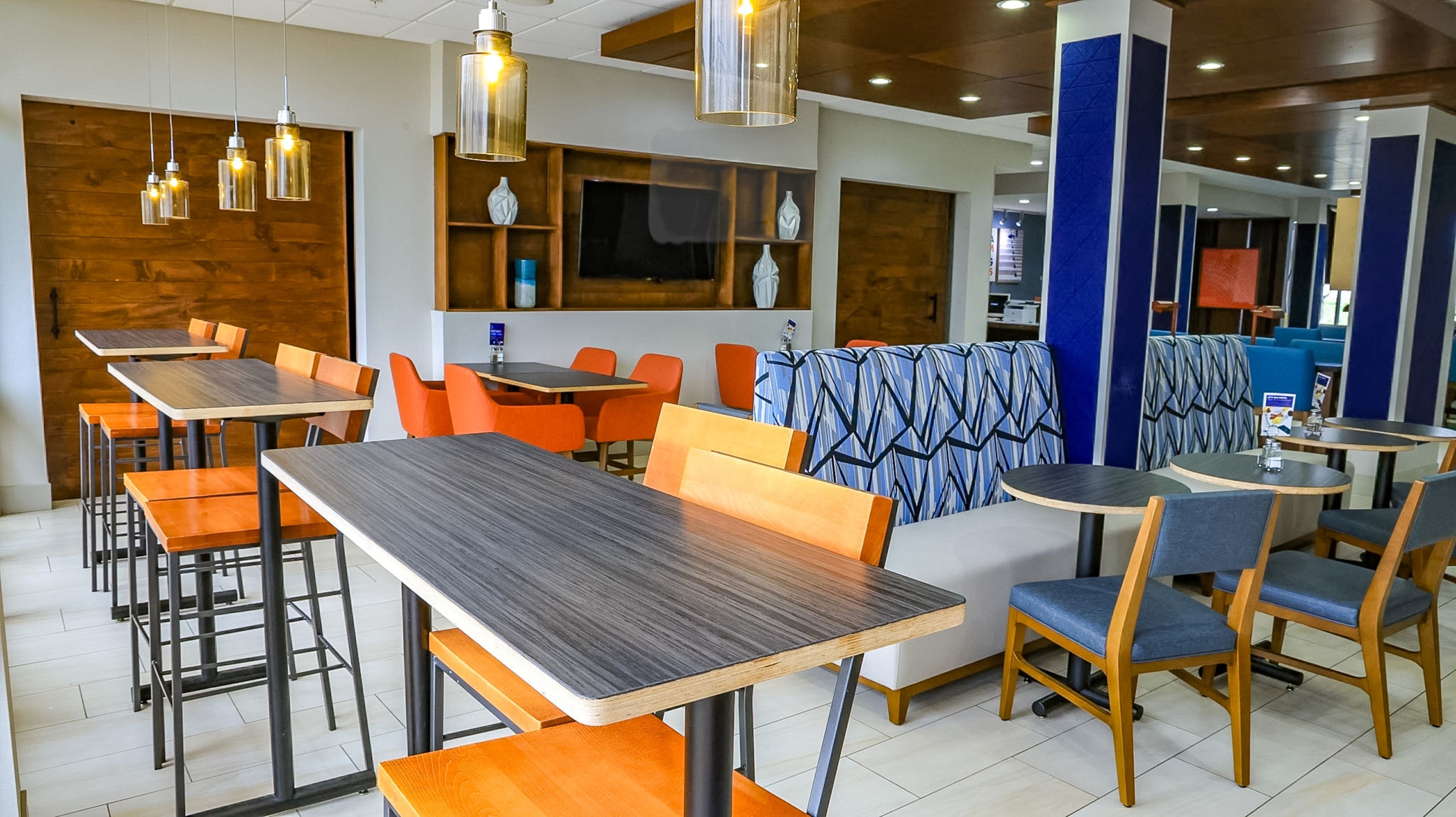 A modern restaurant interior with wooden tables, orange chairs, and blue patterned booths.