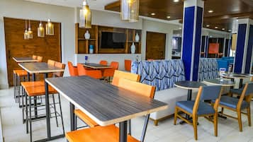 A modern restaurant interior with wooden tables, orange chairs, and blue patterned booths.