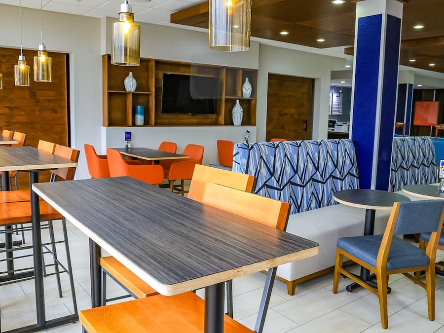 A modern restaurant interior with wooden tables, orange chairs, and blue patterned booths.