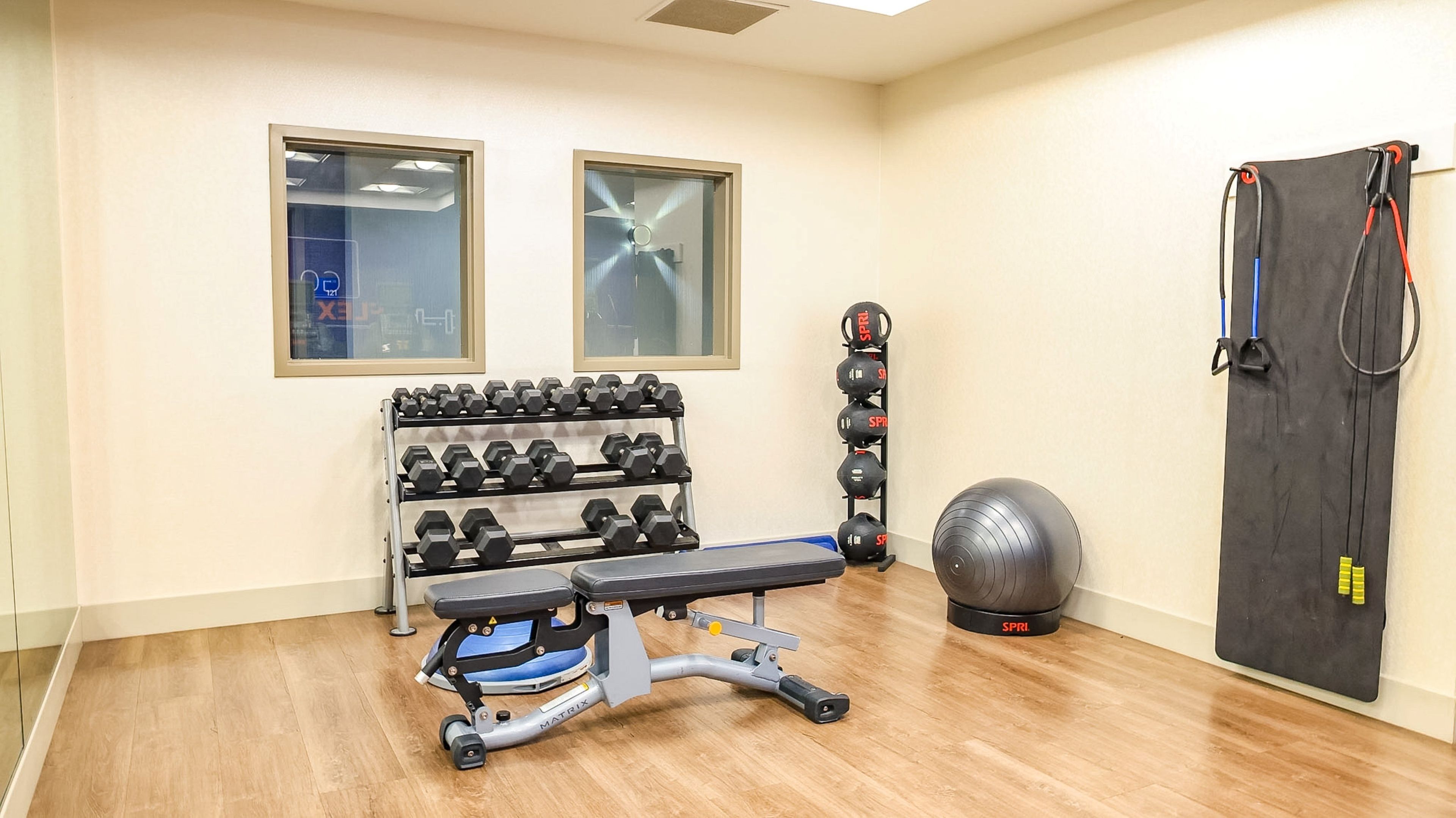 A home gym with a bench, dumbbells, a medicine ball, and resistance bands.