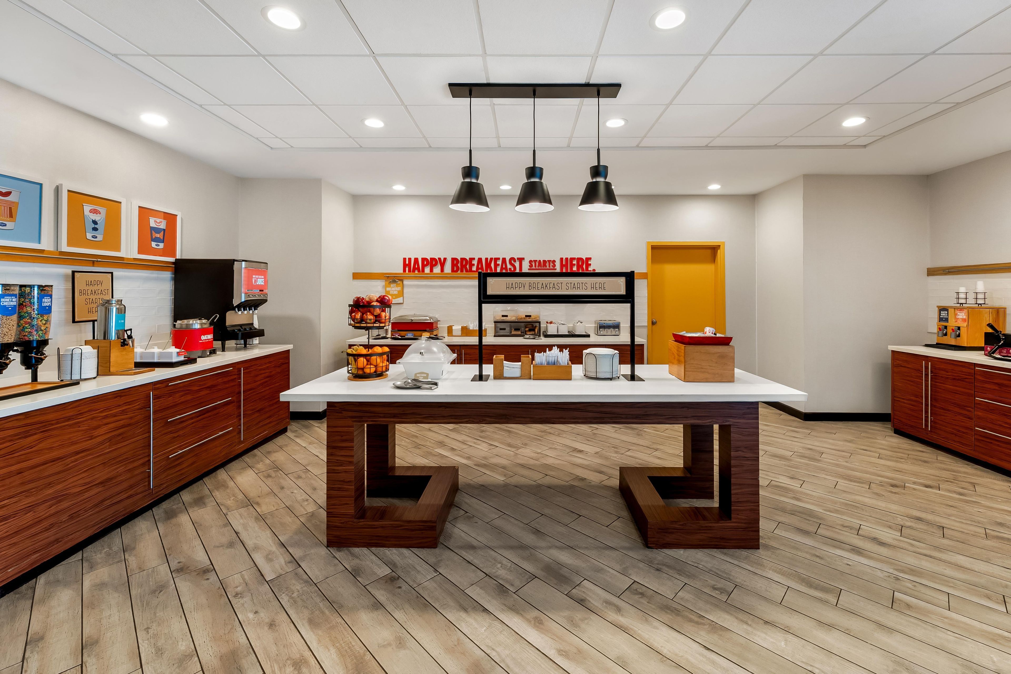 A breakfast area with a central table, coffee machines, and a sign that reads 'HAPPY BREAKFAST STARTS HERE.'