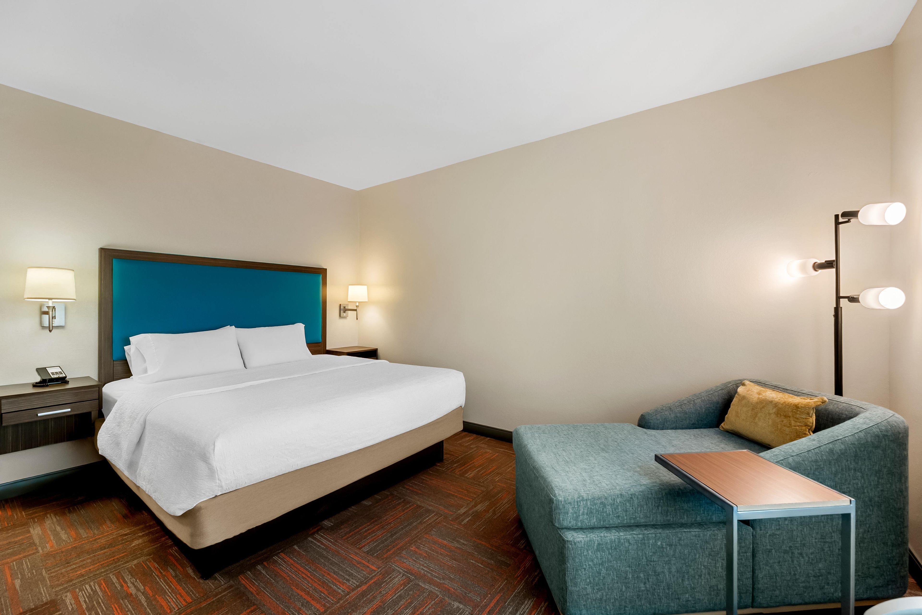 Quarto de hotel com cama, mesa de cabeceira, abajur e um sofá.