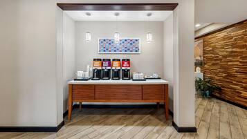 Zona de recepción de un hotel con estación de café que ofrece opciones descafeinado, tueste claro y agua caliente.