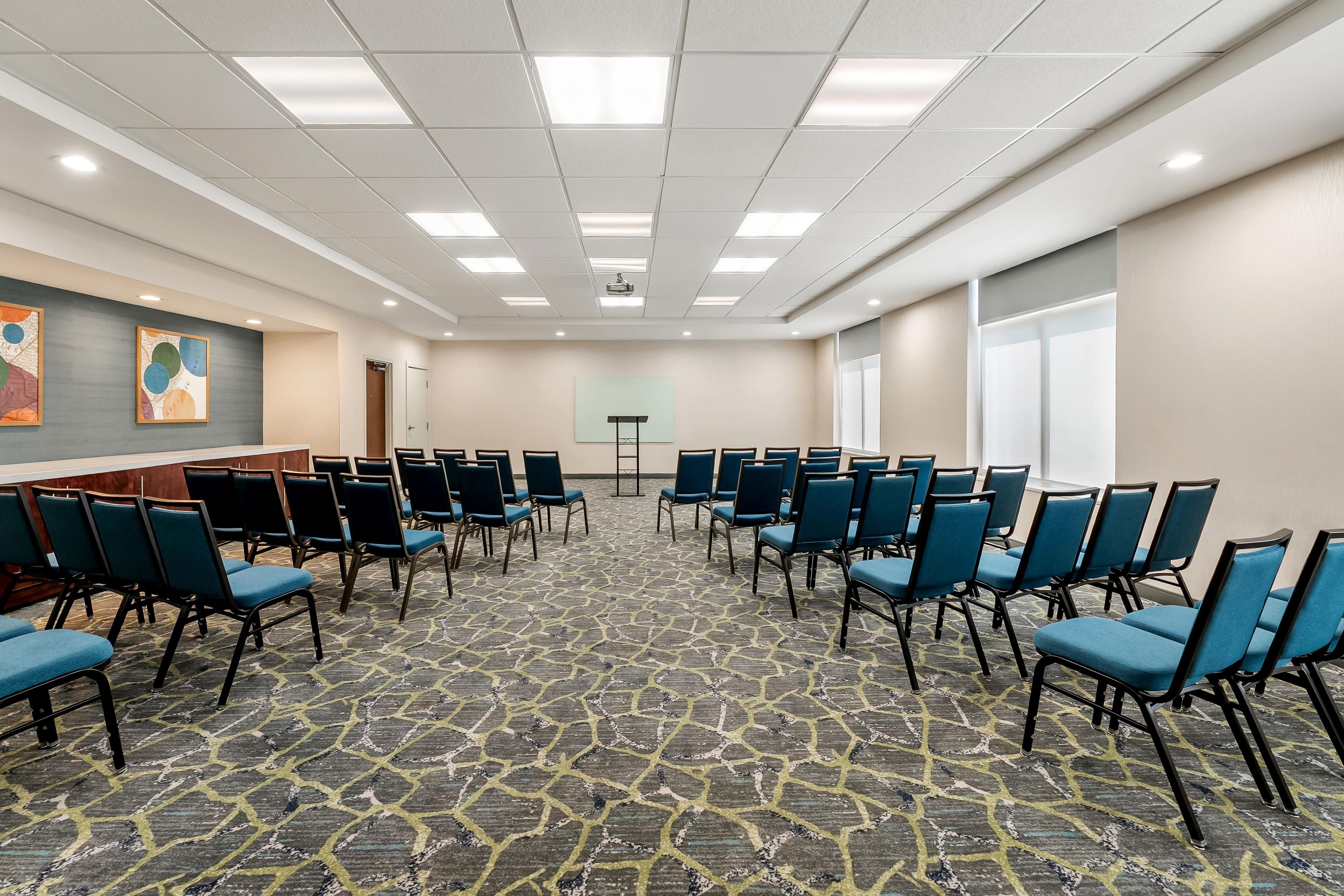 Une salle de conférence avec des rangées de chaises, un écran de projection et un sol recouvert de moquette.