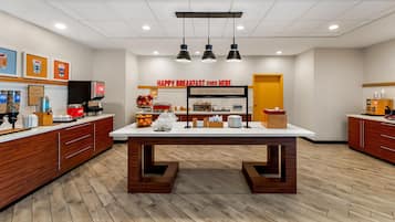 A breakfast area with a central table, coffee machines, and a sign that reads 'HAPPY BREAKFAST STARTS HERE.'
