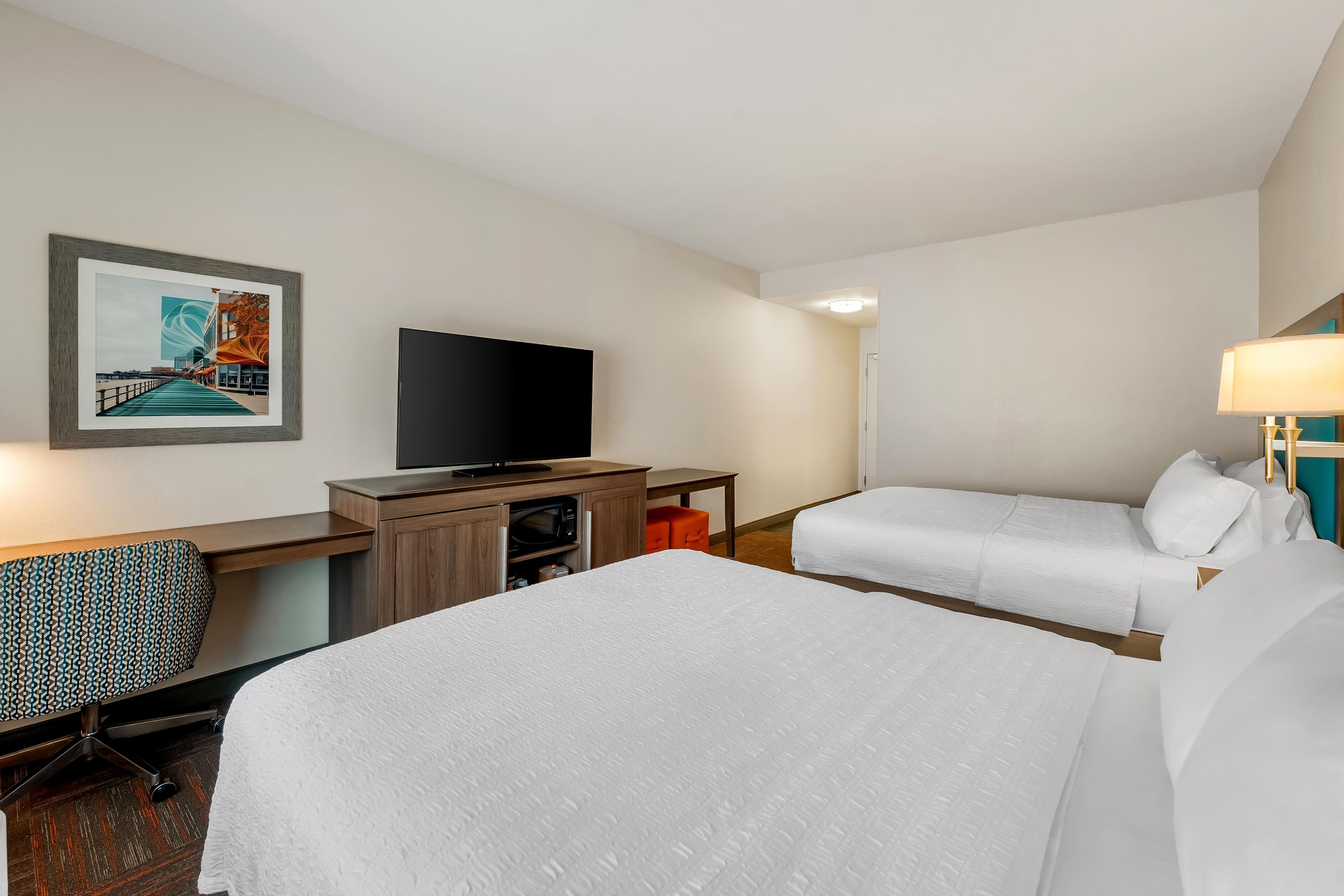 A hotel room with two beds, a desk with a television, a chair, and a framed picture on the wall.