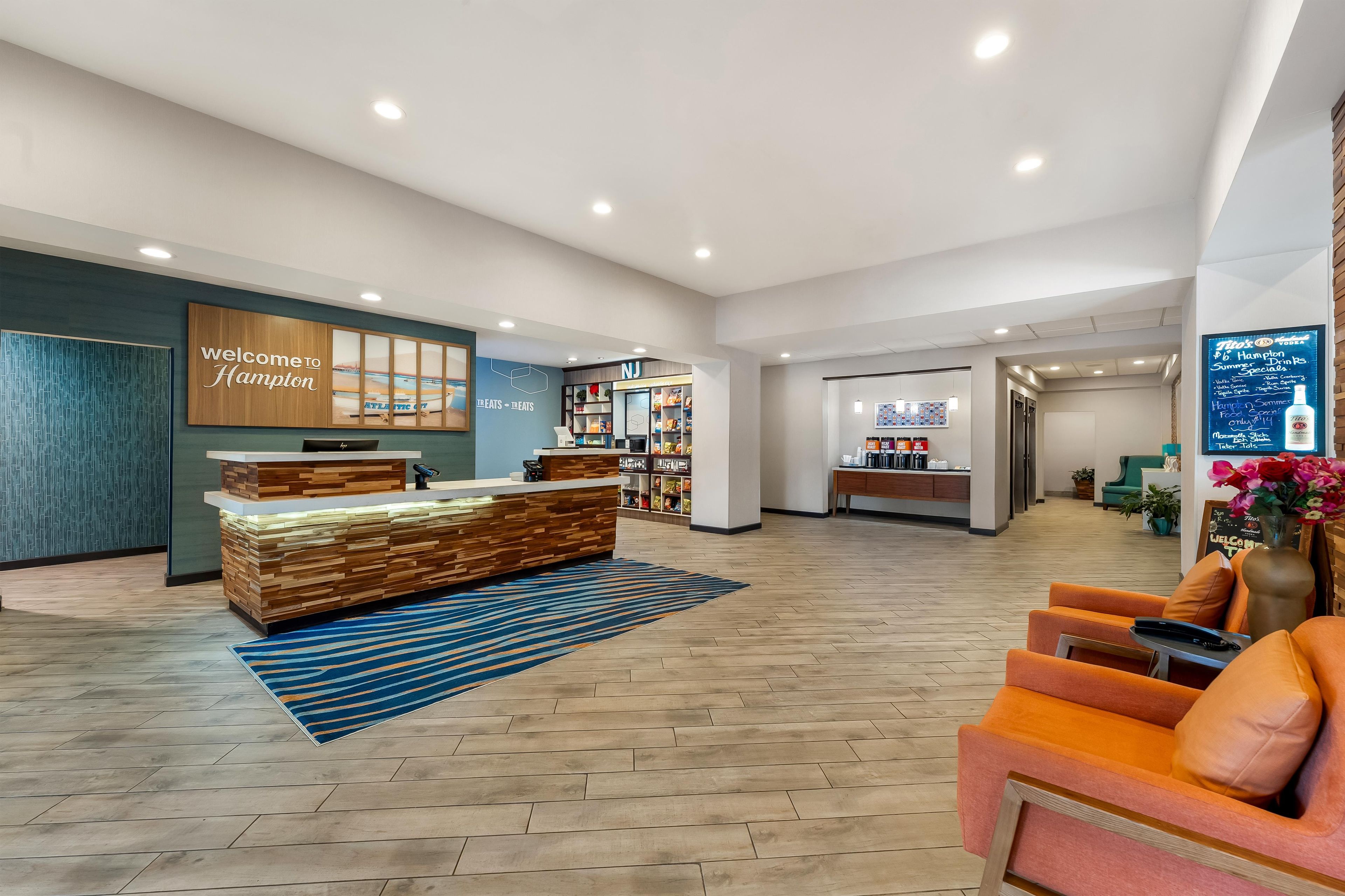 A hotel lobby with a reception desk, seating area, and a wall displaying a welcome sign.