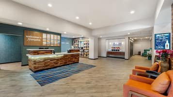 A hotel lobby with a reception desk, seating area, and a wall displaying a welcome sign.
