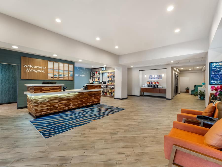 A hotel lobby with a reception desk, seating area, and a wall displaying a welcome sign.