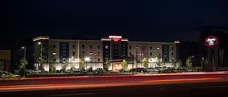 Un hotel Hampton Inn con fachada moderna, varios pisos y una entrada bien iluminada.