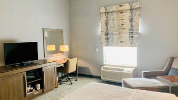 Habitación de hotel con cama, escritorio con silla, televisor, espejo y ventana con persianas.