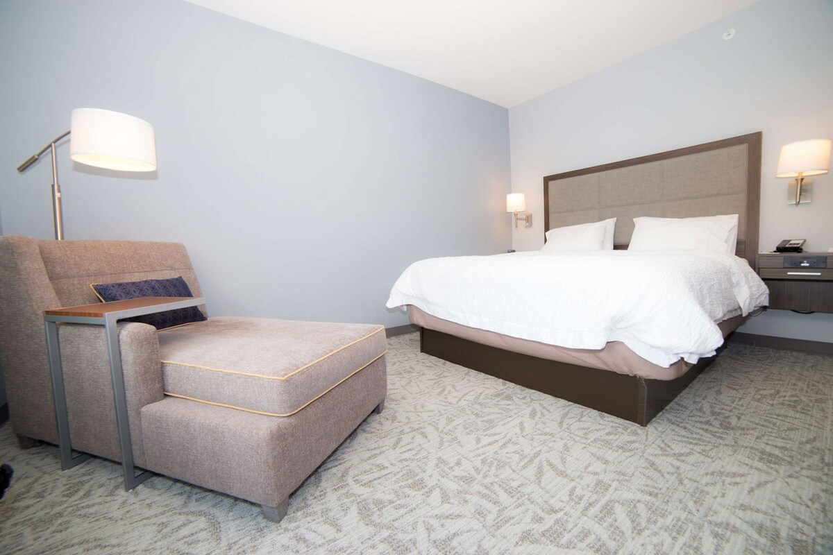 Une chambre d’hôtel avec un lit, une chaise, une table de chevet et une lampe.