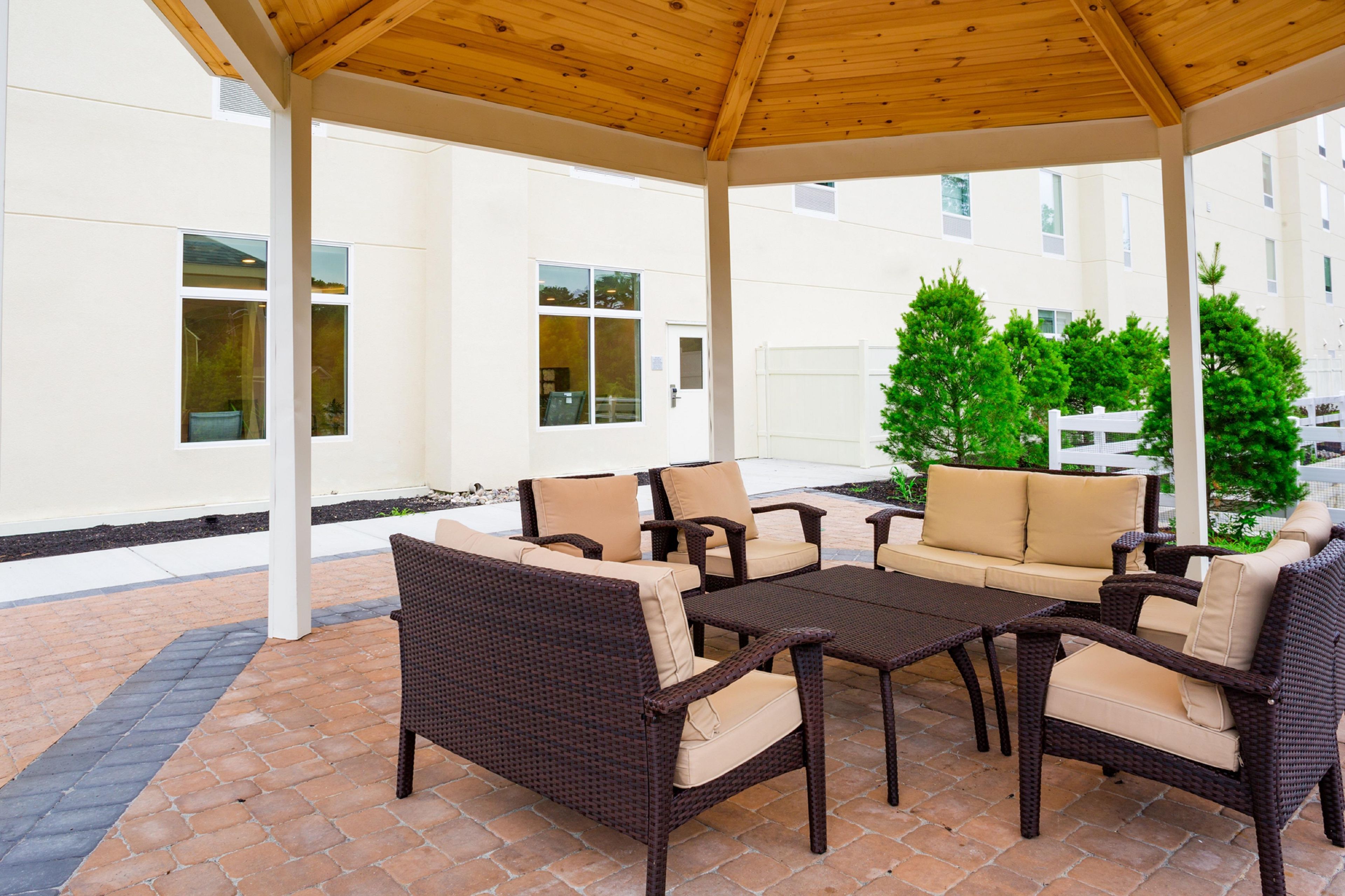 A covered outdoor seating area with wicker furniture and a view of a building in the background.