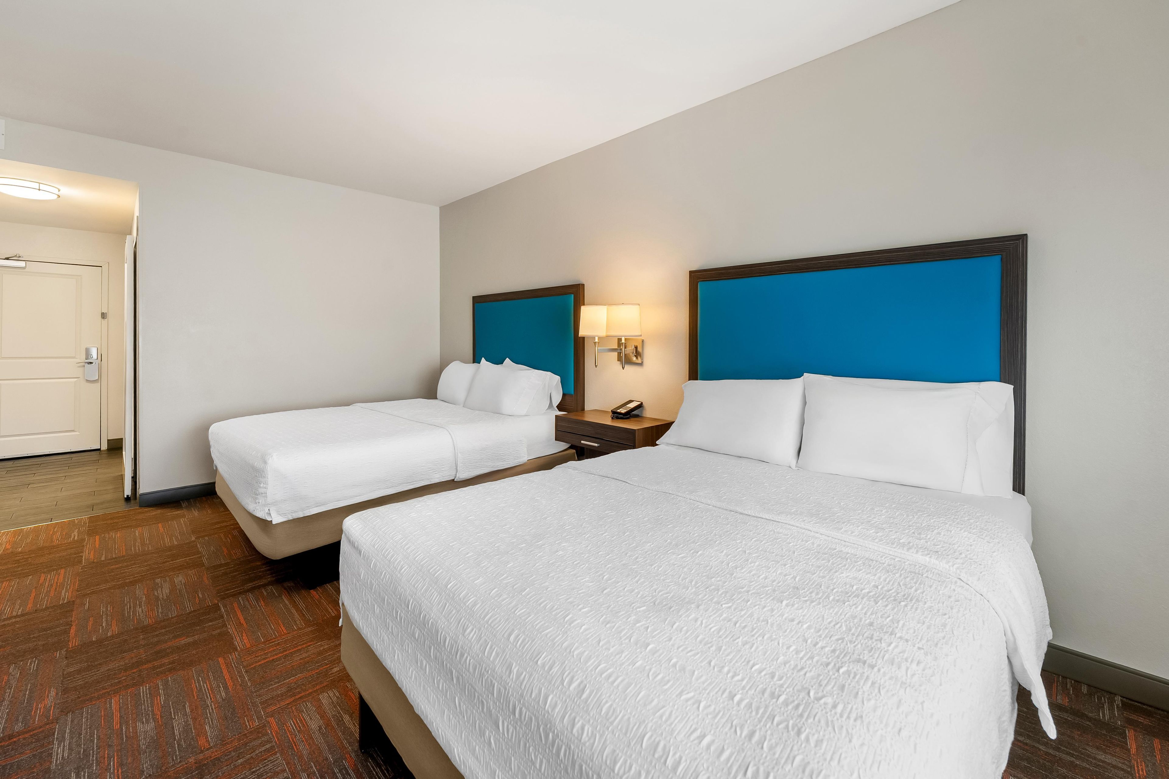 Una habitación de hotel con dos camas, una mesita de noche, una lámpara y una puerta.