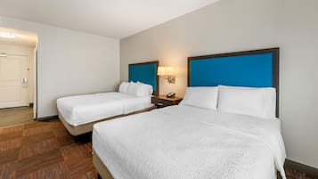 Una habitación de hotel con dos camas, una mesita de noche, una lámpara y una puerta.