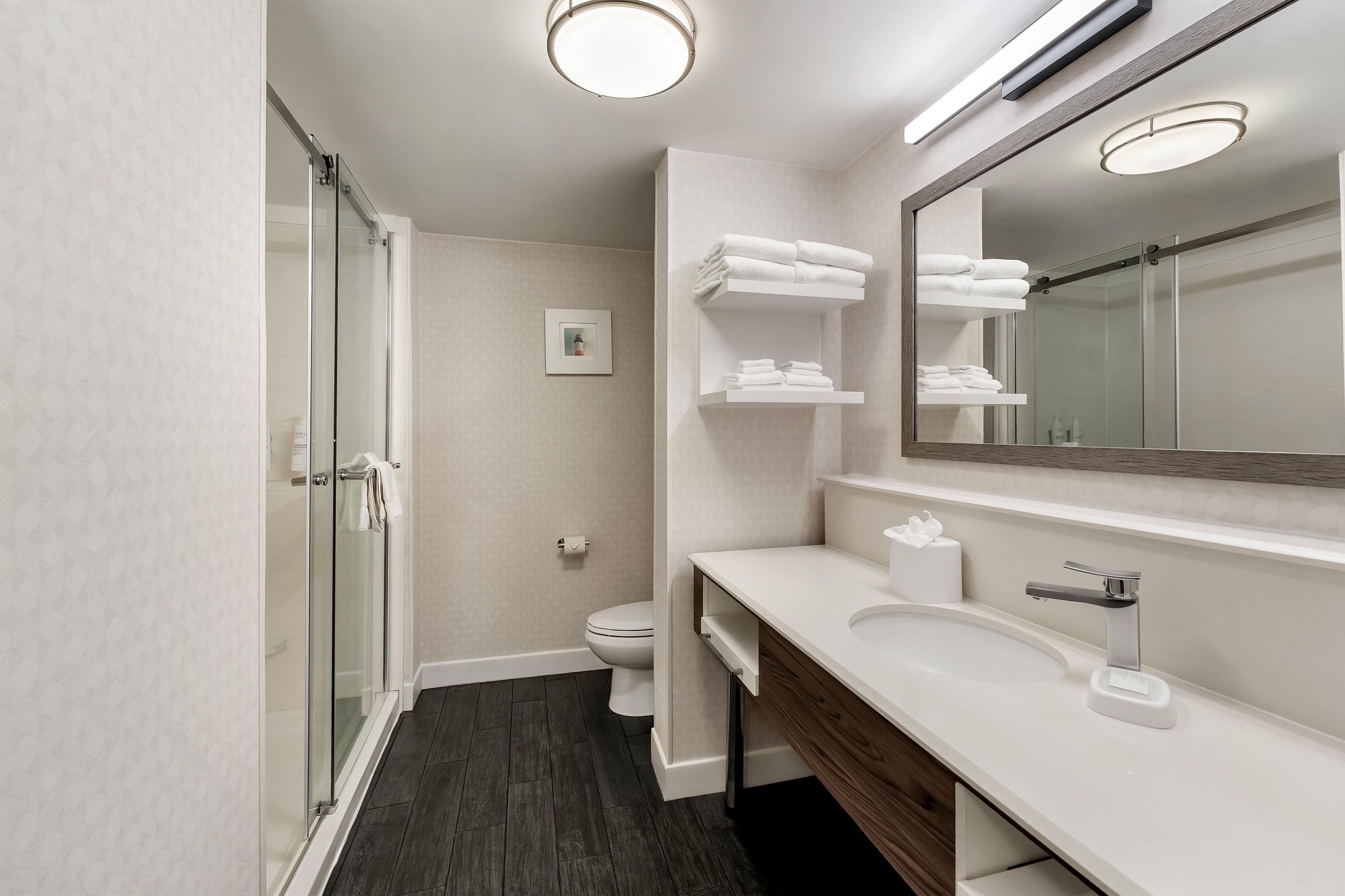 Ein modernes Badezimmer mit Duschkabine aus Glas, Toilette, Waschbecken mit Spiegel und Handtuchhaltern.