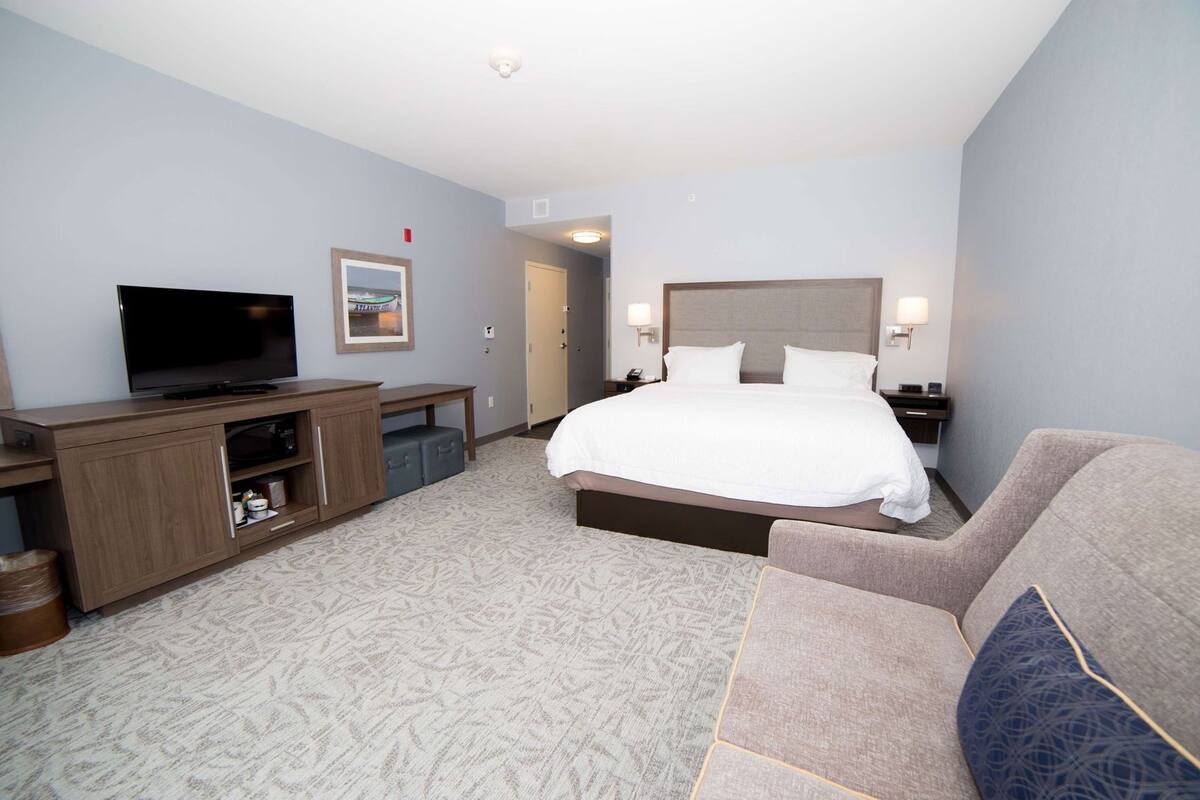 A hotel room with a bed, a TV, a desk, a chair, and a door.