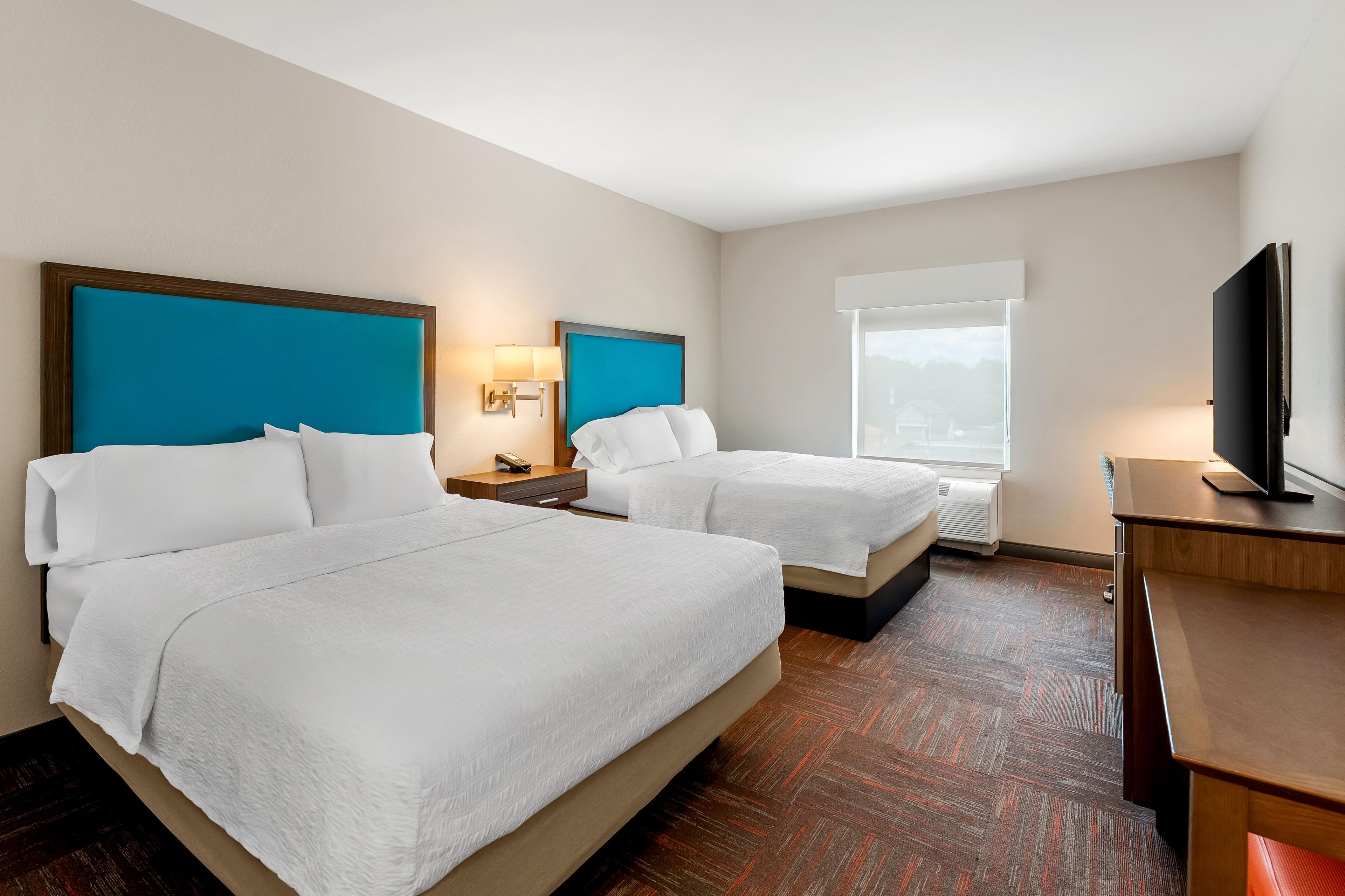 A hotel room with two beds, a desk, a television, and a window.