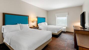 A hotel room with two beds, a desk, a television, and a window.