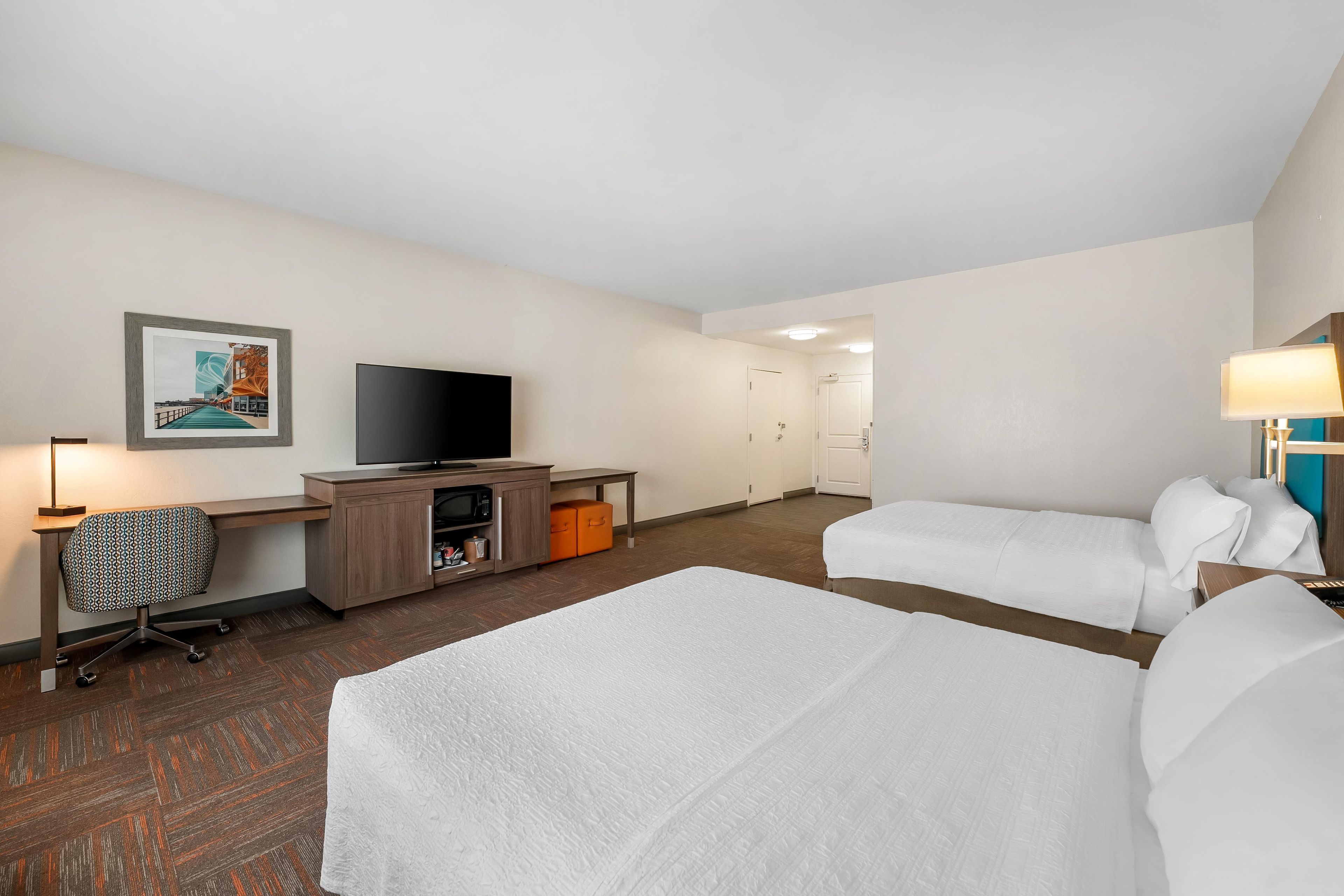 A hotel room with a bed, a desk with a TV, a chair, and a lamp.