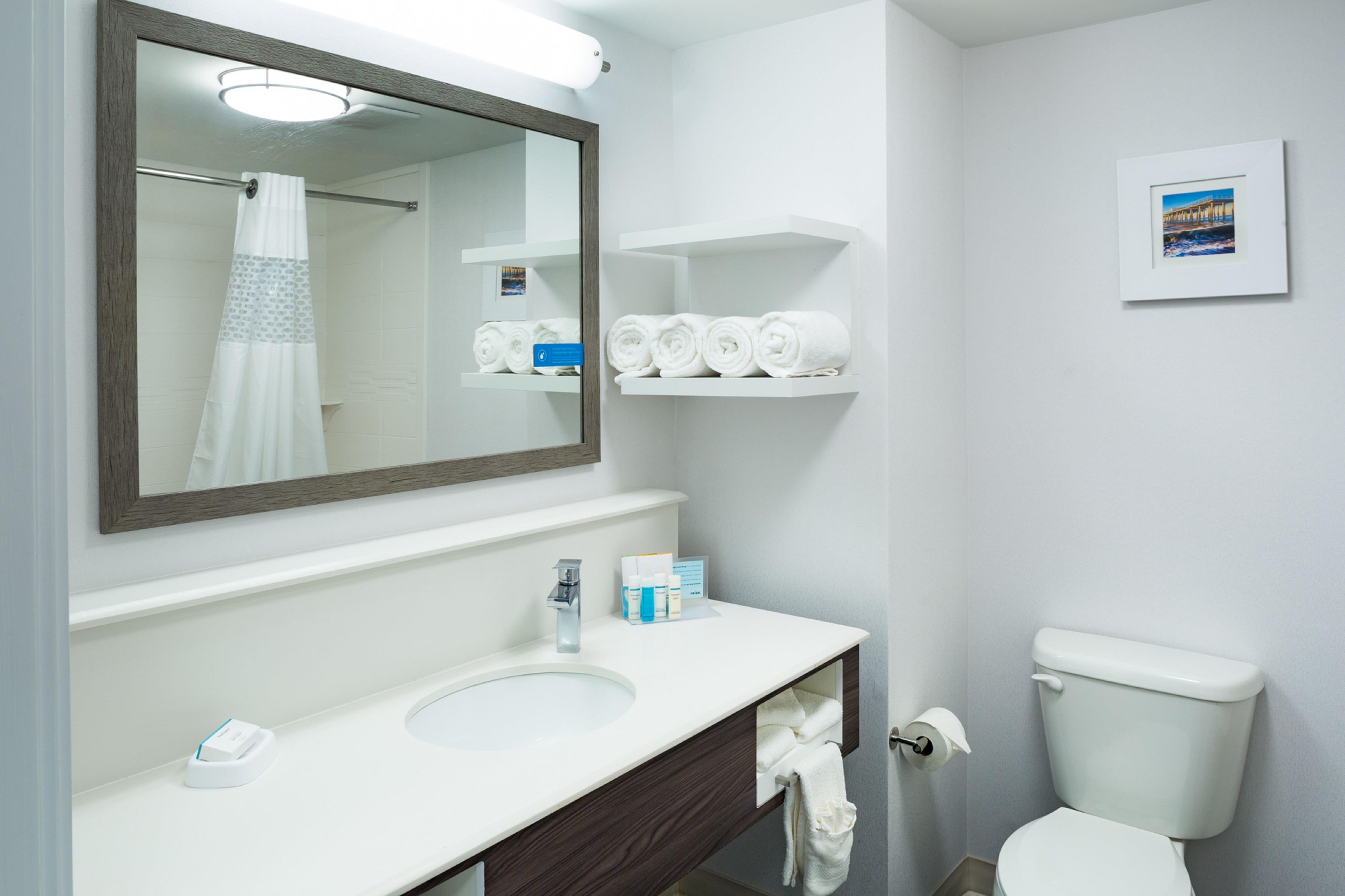 A bathroom with a white sink, a mirror, a toilet, and a shelf with towels.