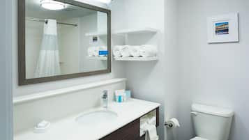 A bathroom with a white sink, a mirror, a toilet, and a shelf with towels.