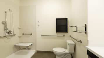 A modern bathroom with a white toilet, grab bars, a shower with a handheld showerhead, and a small shelf.