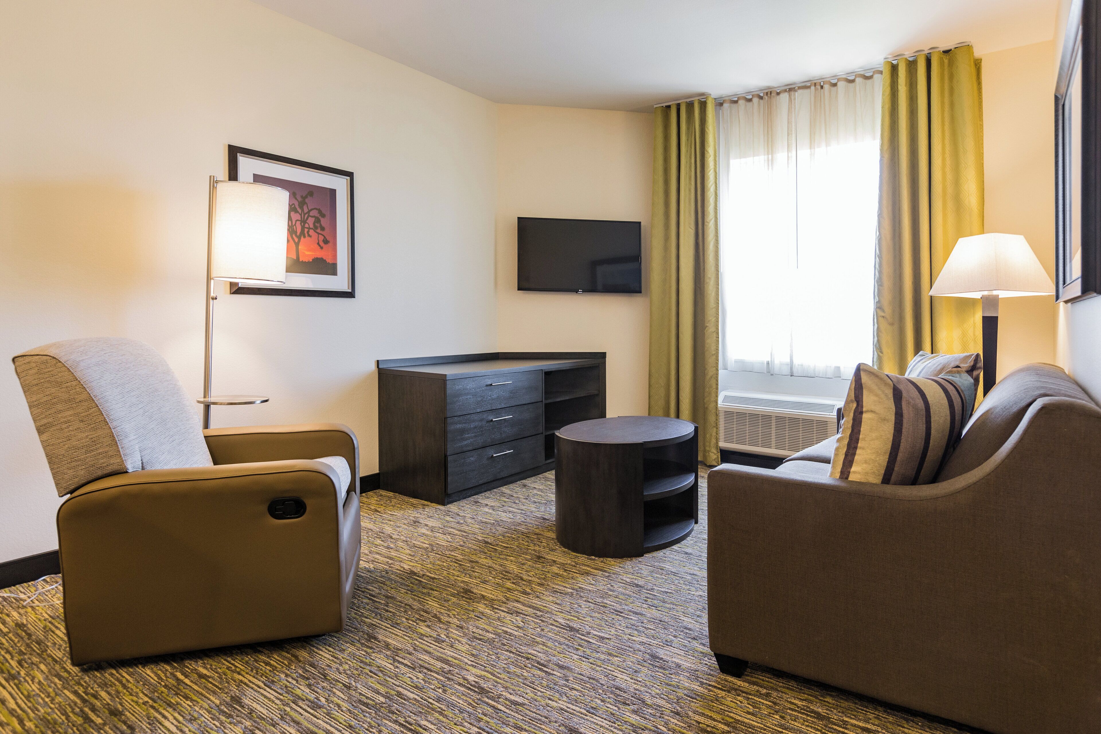 Habitación de hotel con sofá, sillón, televisión y escritorio.