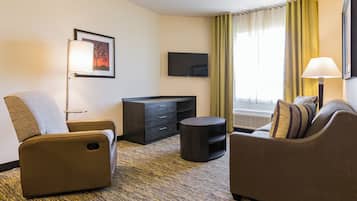Habitación de hotel con sofá, sillón, televisión y escritorio.