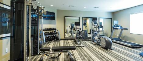 A gym with various exercise equipment, including a weight bench, dumbbells, and cardio machines.