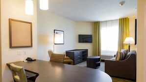 Une chambre d’hôtel avec une table de salle à manger ronde, un canapé, une télévision et une lampe.
